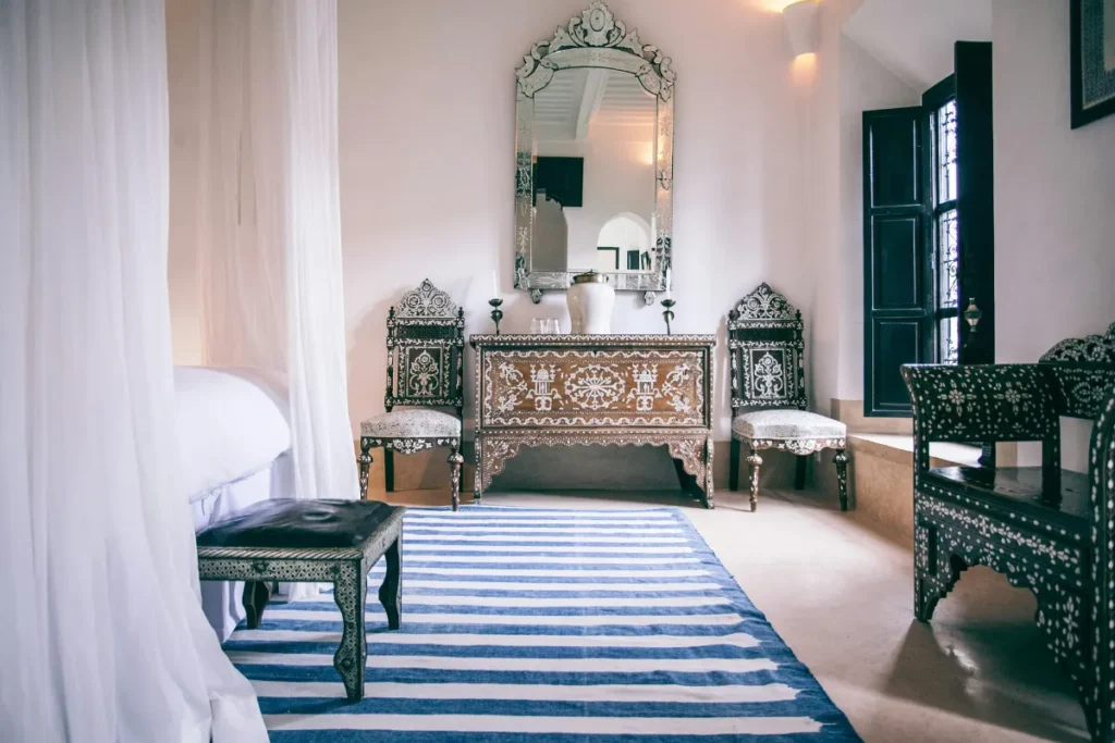 A stylish Moroccan bedroom featuring intricate wooden furniture and a striped white and blue rug